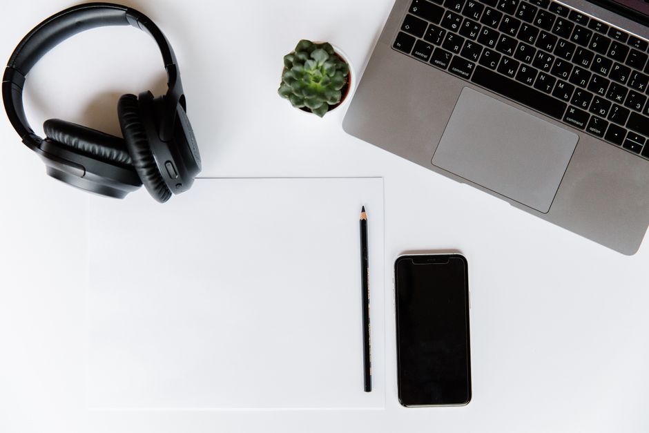 Top view of a modern workspace featuring a laptop, smartphone, headphones, and a pencil.