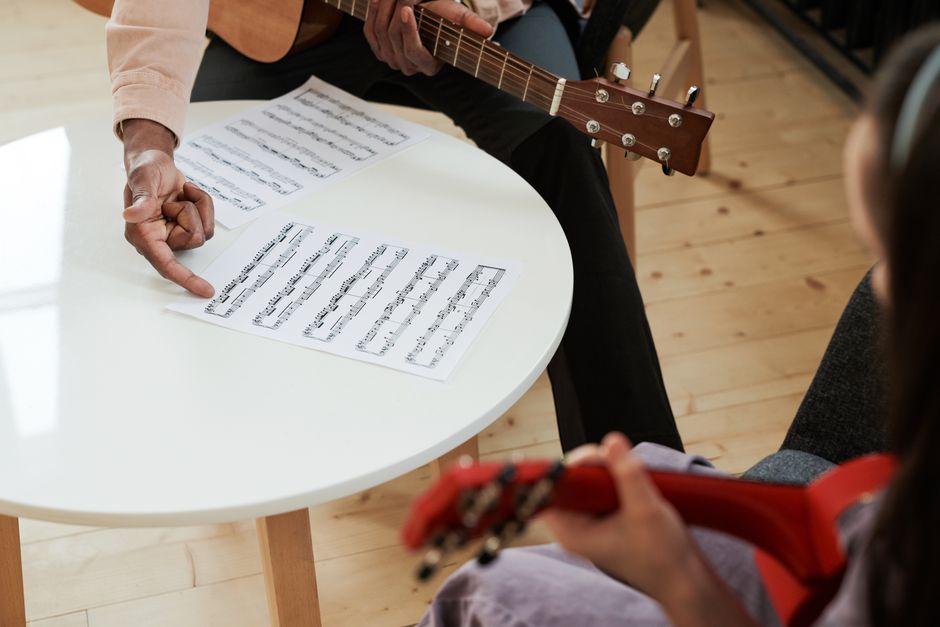Hands demonstrating music on an acoustic guitar with sheet music, ideal for learning concepts.