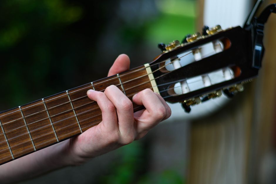Close-up of a hand playing a classical guitar chord outdoors, showcasing finger placement.